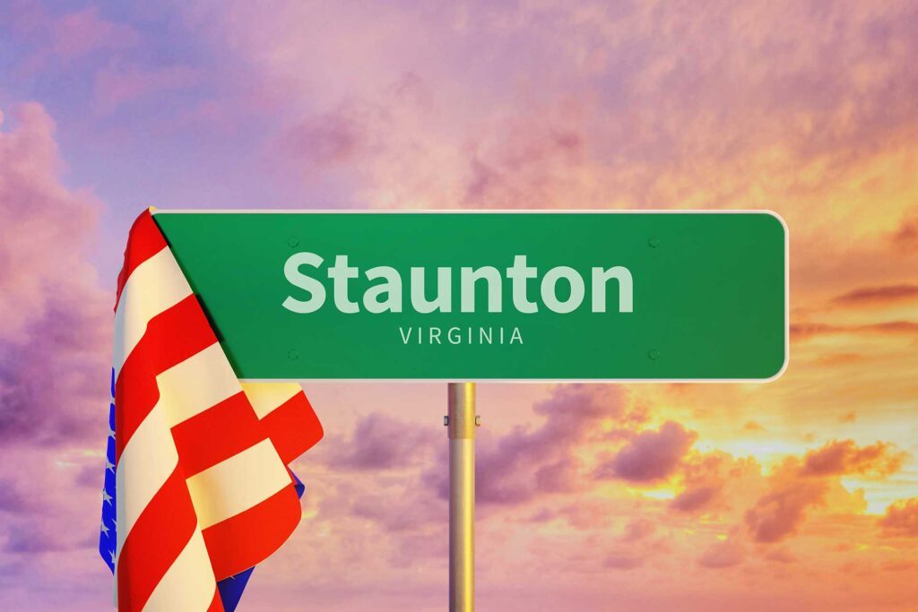 Road sign of Staunton Virginia with an American flag draped over the left corner against a beautiful sunset